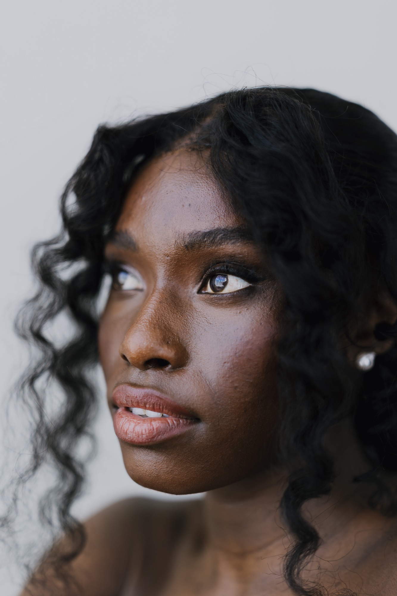 Close-up beauty portrait of a model with curly hair, glowing skin and softly shimmered eye makeup