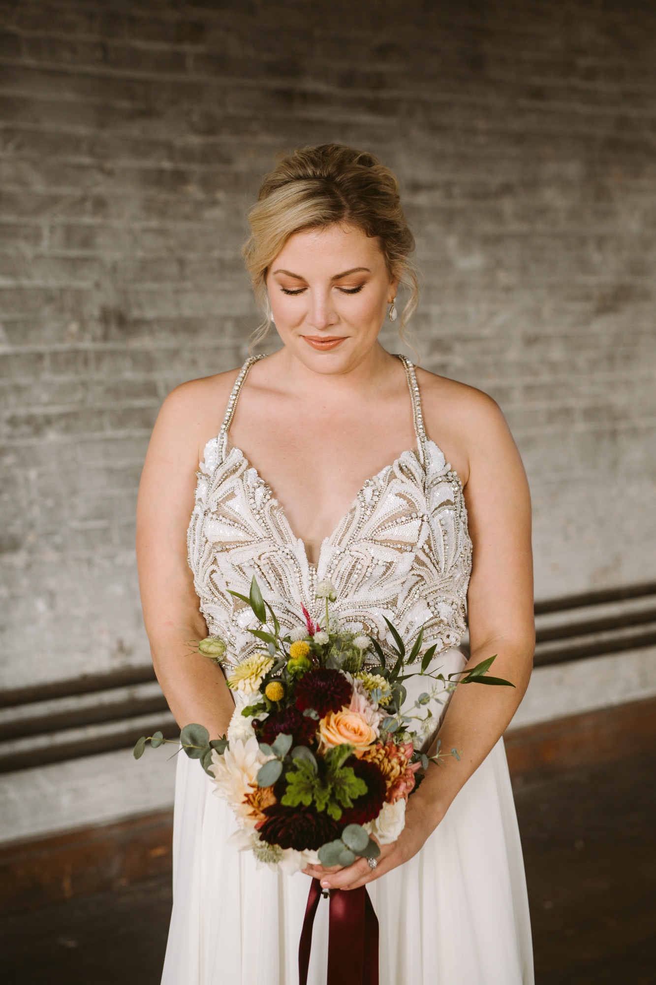 A Glow Charm bride in a beaded gown holding an autumn bouquet, soft natural wedding makeup
